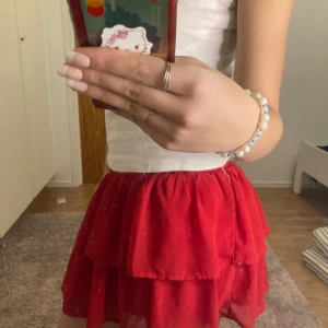 Röd volangkjol - Söt röd kortkjol med volanger, perfekt för sommarens fester. Kjolen har en elastisk midja för bekväm passform och är gjord i ett lätt och luftigt material. Den är idealisk för att skapa en lekfull och romantisk look. Pris kan diskuteras!