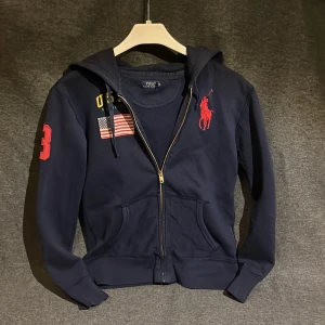 Ralph lauren hoodie blå - Säljer en snygg mörkblå hoodie från Polo Ralph Lauren med dragkedja och luva . Den har en stor röd häst på bröstet, USA-flagga och 3 på ärmen. Skick 7/10, Stl Xs men sitter lite mindre 