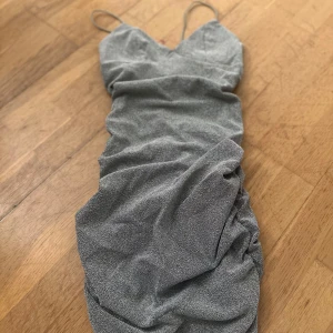 Glittrig klänning med smala axelband - Snygg glittrig klänning i silver med smala axelband och v-ringad design. Klänningen har en åtsittande passform och rynkade detaljer. Köpt på Shein.