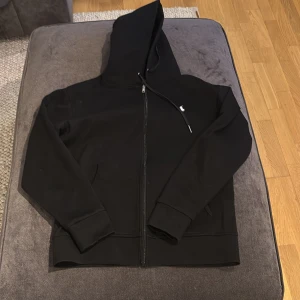 Svart hoodie med dragkedja  - Säljer en stilren svart hoodie från Polo Ralph Lauren. Den har en dragkedja framtill och en liten broderad logga på bröstet. Perfekt för en avslappnad look.