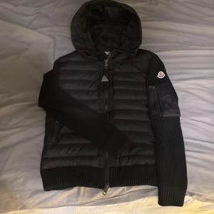 Svart pufferjacka från Moncler - Snygg svart cardigan från Moncler med huva och dragkedja. Perfekt för våren. Skriv vid några funderingar!