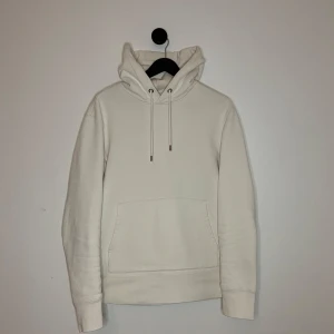 J.Lindeberg Hoodie - Säljer en stilren vit hoodie från J.Lindeberg. Den har en klassisk design med dragsko i huvan och en praktisk magficka. Perfekt för en avslappnad look. Hör gärna av er vid flera frågor eller funderingar! 