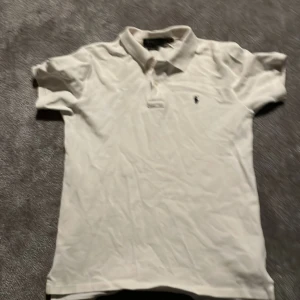 Vit pikétröja från Ralph Lauren  !! PRISET EJ HUGGET I STEN!! - Storlek 10/12 M  sitter större  knappt använd säljer för att den inte passar och inte kommit till användning på länge                    OBS!! PRISET EJ HUGGET I STEN