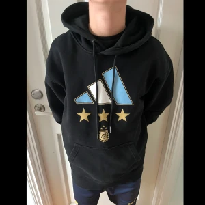 Svart hoodie med Messi-tryck - Säljer en svart hoodie från Adidas med stort tryck av Messi och nummer 10 på ryggen. Framsidan har det argentinska landslagets emblem och tre stjärnor. Perfekt för fotbollsfans! 🖤