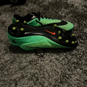 Gröna fotbollsskor från Nike - Snygga gröna fotbollsskor från Nike med svarta detaljer och en cool dödskalle på sidan. Skorna har snörning och är designade för optimal prestanda på planen.  