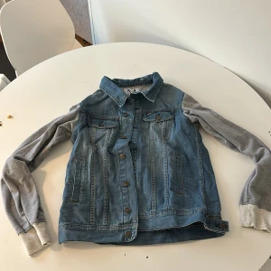 Jeansjacka med grå ärmar - Snygg jeansjacka från Zalando med gråa, mjuka ärmar i sweatshirtmaterial. Jackan har knappar framtill och två bröstfickor med lock. Perfekt för en avslappnad stil.