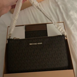 HELT NY MICHAEL KORS VÄSKA - Snygg brun handväska från Michael Kors, man får med matchande kortfodral. Väskan har ett stilrent MK-mönster. Helt ny & oanvänd 💕(Skriv gärna för frågor) Kan diskutera pris vid intresse och SNABB affär!
