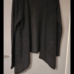 Mörkgrå kofta - Säljer en stilren mörkgrå kofta med långärmad design. Perfekt för lager-på-lager under kyligare dagar. Koftan har en öppen front och är tillverkad i ett mjukt material som ger en bekväm passform.