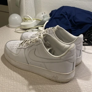 Nike Air Force 1 - Säljer ett par klassiska vita Nike Air Force sneakers. Skorna har en stilren design med snörning och den ikoniska Nike-loggan på sidan. Perfekta för en casual look.