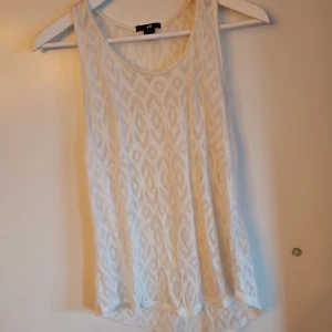Vit mönstrad linnetopp från H&M - Säljer en vit ärmlös linnetopp från H&M med ett subtilt mönster. Perfekt för varma dagar och enkel att matcha med andra plagg. Toppen har en rund halsringning och är tillverkad i ett lätt material.