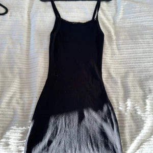 Svart klänning från Brandy Melville - Snygg svart klänning från Brandy Melville med smala axelband och spetsdetaljer vid halsringningen. Perfekt för en stilren look. Klänningen har en tight passform och är tillverkad i ett mjukt material.