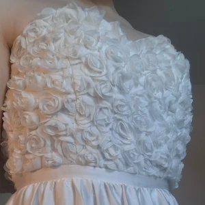 Vit axelbandslös klänning med rosdetaljer - ca 38x2 bröstmått, ca 33x2 midjemått. Jag är 165 cm och klänningen nuddar golvet, kjolen är ca 105 cm. Säljer denna student/bal/festklänning då den tyvärr blivit för liten runt bröstmåttet (jag har C-kupa). Den kommer sitta tightare än på bilden om klänningen passar dig då den inte är knäppt. Har aldrig använt den, endast provat 2 gånger. Inga defekter, helt perfekt. Kjolen är väldigt flowig med silke-material och skön att ha på, med blommor på toppen. Har en blixtkedja där bak! 🌺