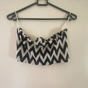 Svartvit mönstrad tubtopp från Vero Moda - Snygg svartvit tubtopp från Vero Moda med ett zigzag-mönster. Perfekt för sommardagar med sin lätta och bekväma design. Toppen har smala axelband och en stilren look.