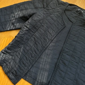 Svart quiltad jacka - Säljer en stilren svart quiltad jacka. Den har en enkel design, vilket ger den en clean look. Perfekt för höst och vår när du vill ha något lätt men ändå snyggt. Jackan har långa ärmar och är både svalt och varmt beroende på vad du har under