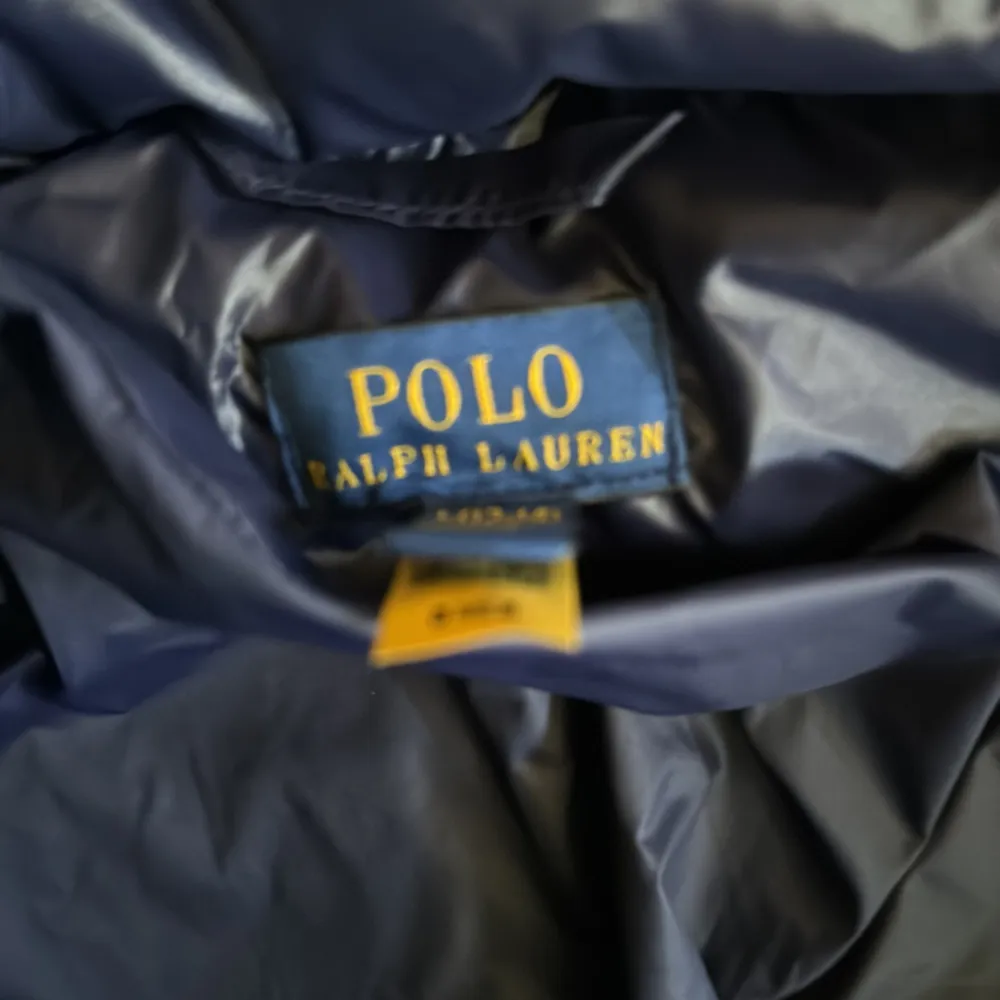 Säljer en snygg och varm mörkblå dunjacka från Polo Ralph Lauren. Jackan har en pufferstil med en praktisk huva och dragkedja framtill. Perfekt för kalla vinterdagar!. Jackor.