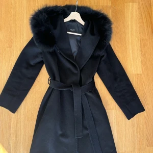 Ullkappa med äkta päls - Svart kappa från Hollies, kappan är i ull och kragen är i äkta päls. Fint skick. Nypris ca 6000kr. 