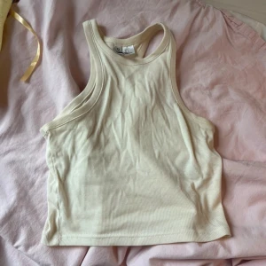 Beige ribbad linnetopp från Divided - Säljer en snygg beige ribbad linnetopp från Divided. Perfekt för sommardagar eller som ett basplagg i garderoben. Toppen är ärmlös och har en skön passform. Använd den som den är eller under en jacka för en lager-på-lager-look.