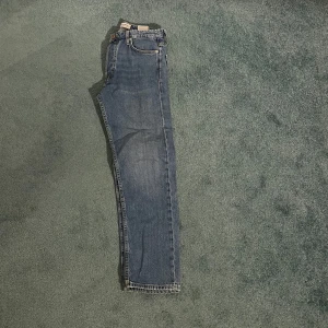 Blå jeans - Säljer ett par klassiska blå jeans i storlek 29/30. De har en straight passform och är i bra skick. Perfekta för vardagsbruk och kan matchas med nästan vad som helst. De har en traditionell femficksdesign och en knappgylf.