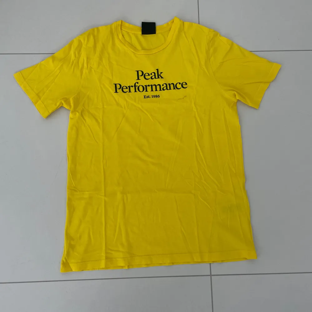 Säljer en snygg gul t-shirt från Peak Performance. Den har en klassisk passform med korta ärmar och ett tryck på framsidan. Perfekt för sommardagar eller som ett färgglatt inslag i garderoben!. T-shirts.