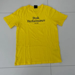 Gul t-shirt från Peak Performance - Säljer en snygg gul t-shirt från Peak Performance. Den har en klassisk passform med korta ärmar och ett tryck på framsidan. Perfekt för sommardagar eller som ett färgglatt inslag i garderoben!