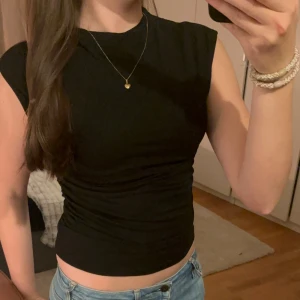 Svart ärmlös topp - Säljer en stilren svart ärmlös topp som är perfekt för både vardag och fest. Toppen har en tight passform och är gjord i ett mjukt och stretchigt material. Den är enkel att matcha med jeans eller kjol för en snygg look.