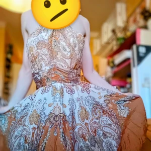 Mönstrad klänning i orange och beige - Säljer en superfin klänning med ett unikt mönster i orange toner. Klänningen har en halterneck-stil och är perfekt för sommarens alla fester. Materialet känns lätt och luftigt, vilket gör den idealisk för varma dagar. Den har en vacker passform som framhäver midjan och ger en elegant siluett. Väldigt retro style. 