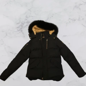 Moose Knuckles - En svart pufferjacka från Moose Knuckles med guldfärgade detaljer och en lyxig guldfärgad insida. Jackan har en avtagbar huva med päls och flera praktiska fickor med dragkedjor. Perfekt för kalla dagar! OBS: jackan passar dig om du är mellan 175-180cm och mellan 65-72kg (den är som en ny)