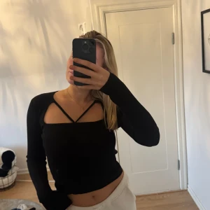 Svart ribbad topp med långa ärmar - Snygg svart ribbad topp med långa ärmar och unik design med korsade band över bröstet. Perfekt för en trendig look.