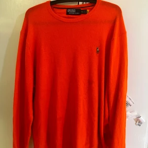 Orange tröja från Polo Ralph Lauren - Säljer en snygg orange tröja från Polo Ralph Lauren med det klassiska broderade logotypen på bröstet. Tröjan har långa ärmar och en rund halsringning. Perfekt för en stilren look!