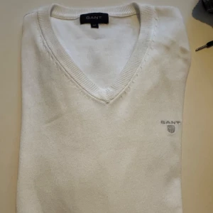 Vit tröja från GANT - Säljer en stilren vit tröja från GANT med v-ringning och broderad logotyp på bröstet. Perfekt för en klassisk och elegant look.