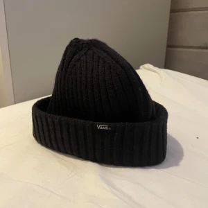Svart ribbad mössa från Vans - Helt oanvänd svart ribbad mössa från Vans. Perfekt för kyliga dagar med stilren design och bekväm passform. Ett måste för garderoben!