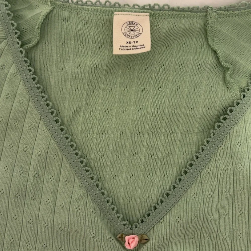 Söt grön topp från Urban Outfitters med v-ringning och spetsdetaljer längs kanten. Toppen har en liten rosa ros framtill och korta ärmar. Perfekt för en avslappnad stil. Endast använd ett fåtal gånger!. Yläosat.