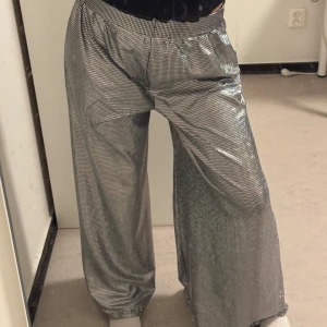 Glittriga vida byxor - Snygga glittriga byxor i silver med en loose passform. Perfekta för att sticka ut på festen! Byxorna har en hög midja och vida ben som ger en cool och trendig look.