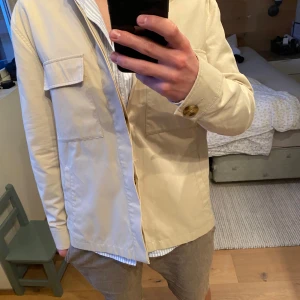 Beige overshirt - Snygg beige overshirt från Sand cobenhagen med knappar och praktiska fickor. Perfekt for alle type klesstiler. Nypris: 3200kr/sek. Pent brukt, ingen bruksmerker. Str 48/M. Dm for flere bilder.  