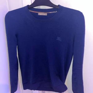 Blå kashmirtröja från Burberry - Snygg blå tröja från Burberry i 100% kashmir. Den har en klassisk rund hals och långa , Står att de är en stlk S men skulle säga XS för den e väldig liten i storleken och sitter väldigt slimfit , tröjan ligger på 5000:- nypris och kashmiren är i fint skick och allt