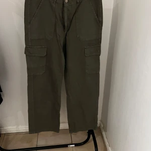 Olivgröna cargobyxor från Zara - Säljer ett par olivgröna cargobyxor från Zara. Byxorna har flera praktiska fickor och en knappstängning framtill. Perfekta för en avslappnad stil med en loose passform.