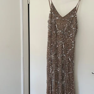 Champagnefärgad paljettklänning - Elegant långklänning i champagnefärg med tunna axelband och v-ringning. Klänningen är täckt av glittrande paljetter som ger en lyxig känsla. Perfekt för festliga tillfällen. Köpt från Asos. 
