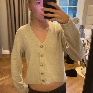 Beige kofta med knappar - Säljer en mysig beige kofta med knappar framtill. Från Zara,Koftan har en v-ringad design och långa ärmar, perfekt för kyligare dagar. Den är ribbad vid ärmslut och nederkant för extra komfort. Storlek s men sitter som en S