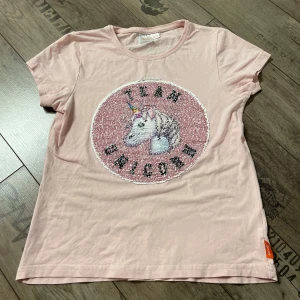 Rosa t-shirt med paljetter och enhörning/panda motiv - Söt rosa t-shirt med korta ärmar och ett unikt paljettmotiv som kan ändras mellan en enhörning och en panda. Perfekt för att lägga till lite magi i vardagen!