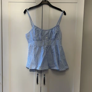 Blå- och vitrandig linnetopp - Säljer en söt blå- och vitrandig linnetopp med knappar framtill. Toppen har smala axelband och en luftig passform, perfekt för varma dagar.