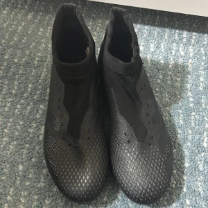 Svarta fotbollsskor från Adidas - Snygga svarta fotbollsskor från Adidas med en strumpliknande passform. Skorna har en texturerad yta för bättre grepp och kontroll på planen. Perfekta för fotbollsspelare som vill ha stil och funktionalitet.