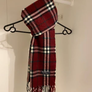 Burberry - Säljer nu denna snygga halsduk ifrån Burberry i burgendy röd. Den Tillverkad i 100% mjuk lammull. Den är i mycket fint skick utan defekter. Perfekt för att hålla dig varm och stilren under kyliga dagar.