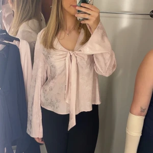 Rosa blus från Gina Tricot - Säljer en ljusrosa blus från Gina Tricot med fin blommig textur. Blusen har långa ärmar och en knytning framtill.  Perfekt till fest eller sommar💕 Använd endast 2 gånger så som ny💕 Nypris 350 ungefär💕