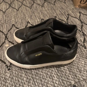 Svarta sneakers från Axel Arigato - Snygga svarta sneakers från Axel Arigato med en stilren design. Skorna har en vit sula och är tillverkade i skinn. Perfekta för en minimalistisk look.
