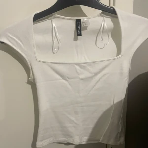 Vit kortärmad topp från H&M - Snygg vit topp från Cosmic med korta ärmar och fyrkantig halsringning. Perfekt för en stilren look.