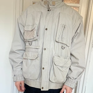 Armyjacka beige  - Säljer en beige vintage armyjacka med flera praktiska fickor och knappar. Jackan har en hög krage och ribbade muddar vid ärmsluten. Perfekt för dig som gillar en funktionell och stilren look. Storlek L. Se mina övriga annonser för fler grymma plagg! 
