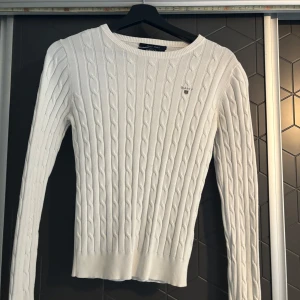 Vit stickad tröja från Gant - Säljer en stilren vit stickad tröja från Gant med kabelstickat mönster. Tröjan har en rund halsringning och långa ärmar, perfekt för kyligare dagar. Den är både bekväm och snygg, ett måste i garderoben! 🧶