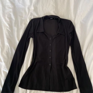 Svart ribbad tröja från Bik Bok - Snygg svart ribbad tröja från Bik Bok i storlek XS. Tröjan har långa ärmar och knappar framtill, vilket ger en stilren look. Perfekt för en chic och enkel stil.