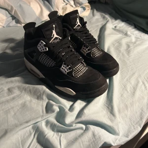 Jordan 4 white thunder - Snygga svarta sneakers med vita detaljer och snörning. Skorna har en ikonisk design med Jumpman-logga på tungan och hälen. Perfekta för en stilren look. Ingen box