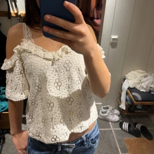 Vit spetsblus med volangdetaljer - Säljer en söt vit spetsblus med offshoulder-design och volangdetaljer. Blusen har korta ärmar och ett vackert spetsmönster som ger en romantisk känsla. Perfekt för sommarens varma dagar. Tycker den är jättefin men kommer inte till användning längre. Den har lite skavanker som ni ser men inget som stör när han har på sig den!!💓💓